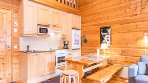 A cozy cabin-style kitchen with wooden cabinets, a microwave, a stove, and a dining area with a bench and table. - Rukansyli 1 by Interhome (Kuusamo)