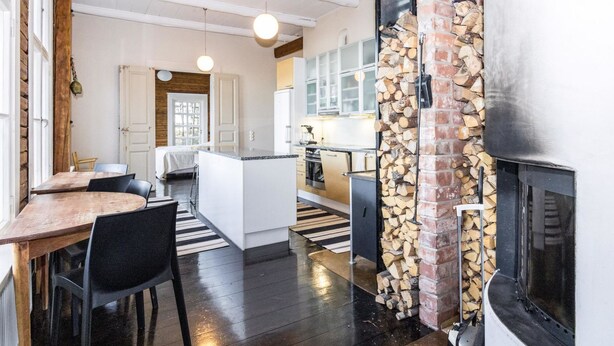 A modern kitchen with a central island, a dining area with a wooden table and chairs, and a fireplace with a stone wall. - Säikkäranta by Interhome (Oulunsalo)
