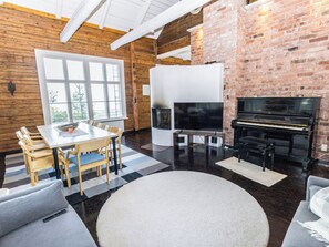 A spacious living area with a fireplace, a piano, a television, and a dining table with chairs.
