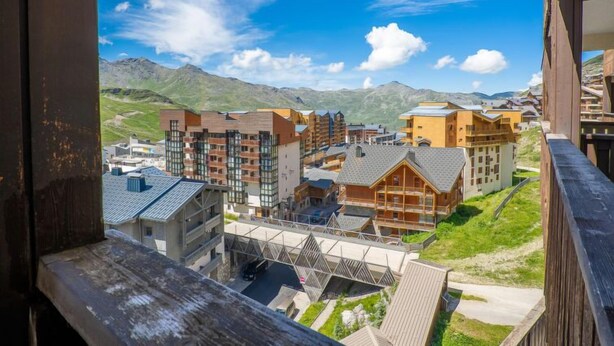 Un moderno complejo hotelero con varias edificaciones, incluyendo una estructura de madera destacada con techo inclinado, frente a un telón de fondo de montañas y cielo azul despejado.