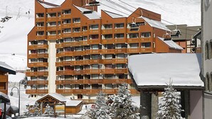 Un hotel de varios pisos con balcones, cables de telesilla y árboles cubiertos de nieve.