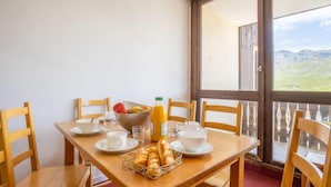 Comedor con mesa de madera dispuesta para el desayuno, con cruasanes, fruta y jugo.