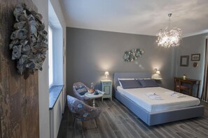 A bedroom with a large bed, a chair, a small table, and a decorative wall piece. - Il Bosco Delle Torte (Castellinaldo)