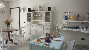 A dining area with a round table, chairs, a cabinet with glass doors, and a shelf with various items. - Il Bosco Delle Torte (Castellinaldo)