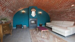 A cozy room with a brick ceiling, a fireplace, a white sofa, and a wooden table. - Il Bosco Delle Torte (Castellinaldo)