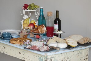 A table with various food items, including bread, cheese, and meats, along with bottles of wine and a fruit basket. - Il Bosco Delle Torte (Castellinaldo)