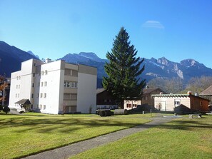 A building with a flat roof and multiple windows, surrounded by a grassy area and a large evergreen tree.