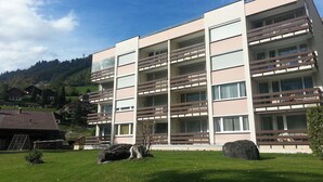 A multi-story building with balconies, a grassy area in front, and a mountainous background. - Neuschwändi 66 Appartement/Fewo 4-Bettwohnung by Interhome (Engelberg)