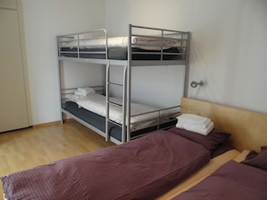 A bunk bed with a lower bunk and a single bed with a purple blanket.