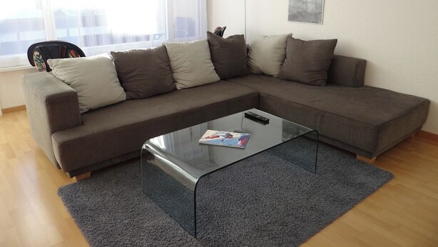 A modern living room with a grey sectional sofa, a glass coffee table, and a large window with curtains. - Neuschwändi 66 Appartement/Fewo 4-Bettwohnung by Interhome (Engelberg)