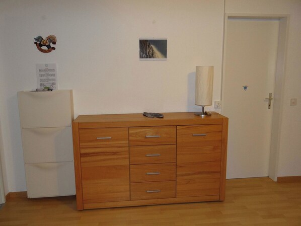 Une pièce avec une commode en bois, un petit tableau encadré accroché au mur et une porte.