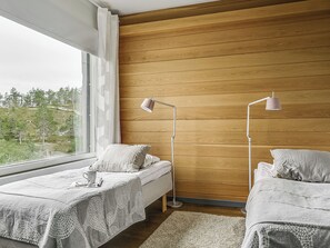 Un dormitorio con dos camas, un ventanal y vistas a árboles.