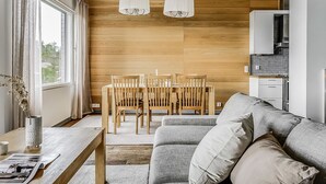 A modern living room with a grey sofa, wooden dining table, and chairs. There are two pendant lights hanging from the ceiling.