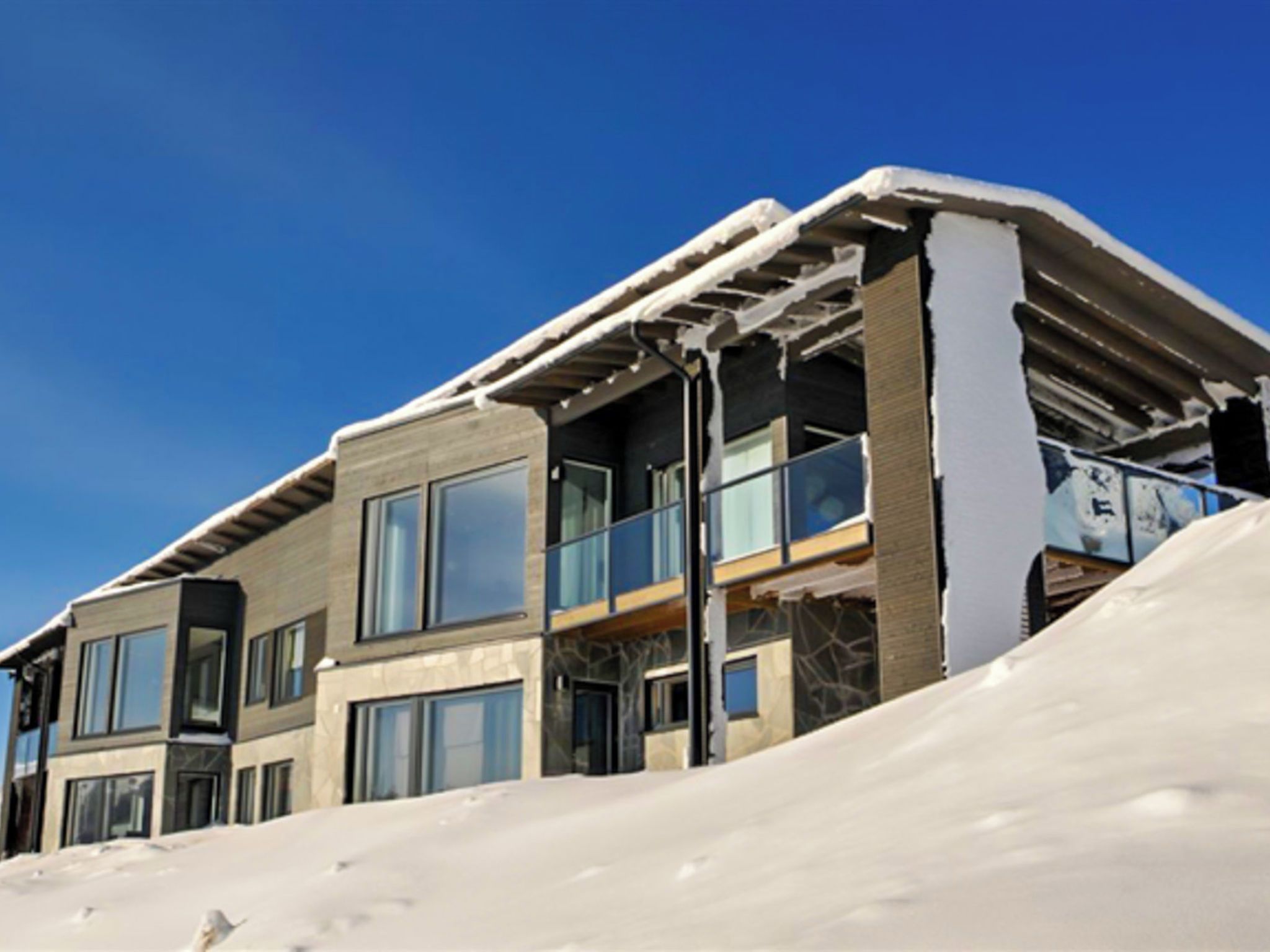 Un immeuble à plusieurs étages, doté de grandes fenêtres et d’un toit recouvert de neige.
