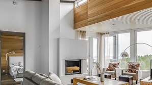A modern living room with a sofa, coffee table, and chairs. There is a fireplace and a large window with a view.