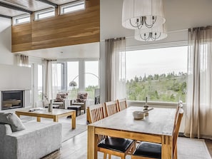 Una sala de estar moderna con comedor, ventanas grandes y vistas a un bosque.