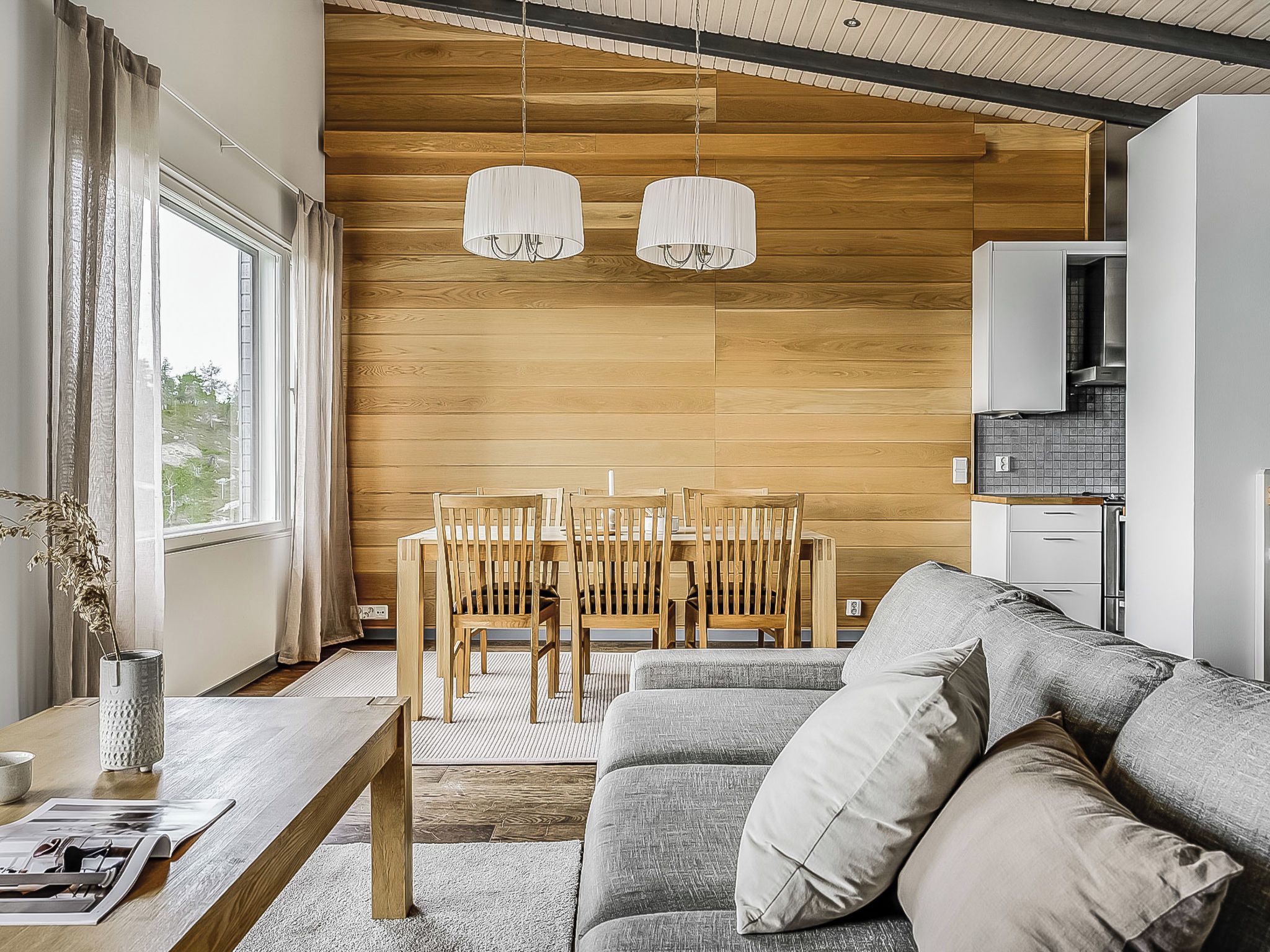 Un salon moderne avec un mur en bois, un canapé gris, une table à manger avec des chaises et des luminaires suspendus.