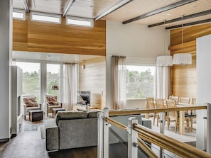 Un interior moderno con techo de madera, ventanas amplias, un sofá, una mesa de comedor y una escalera.