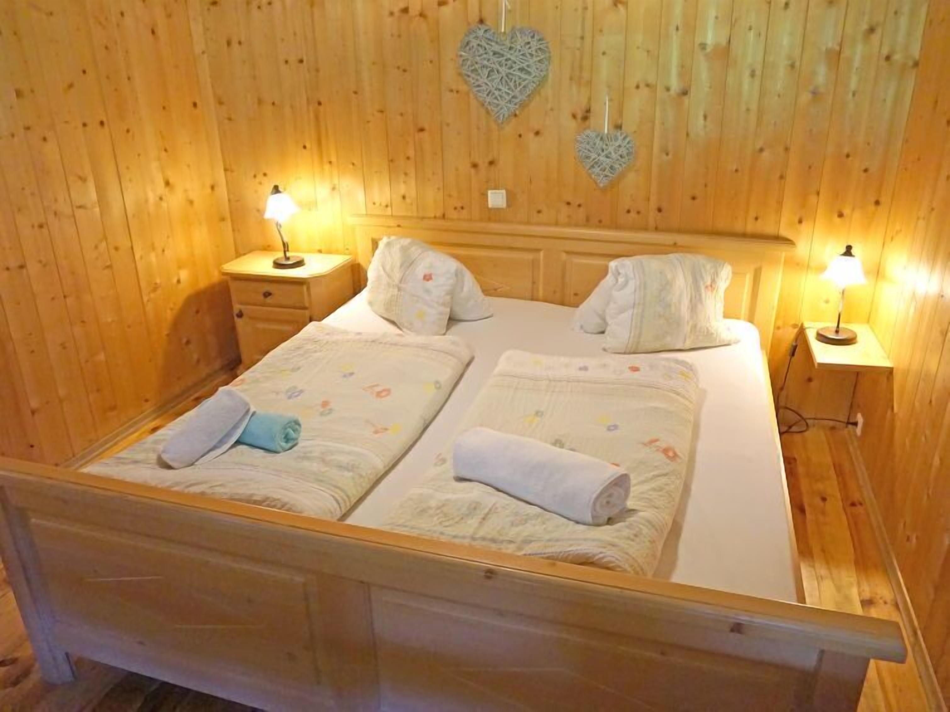 A wooden-paneled room with a double bed, two bedside tables with lamps, and decorative heart-shaped wall hangings.