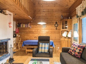 A cozy cabin interior with a dining table, a sofa, a chair, a bookshelf, and a fireplace. - Nurmennunnu by Interhome (Kittilä)