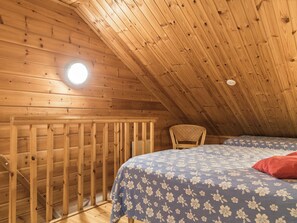 Una habitación de madera con techo inclinado, una cama con ropa de cama floral, una silla y una lámpara circular.