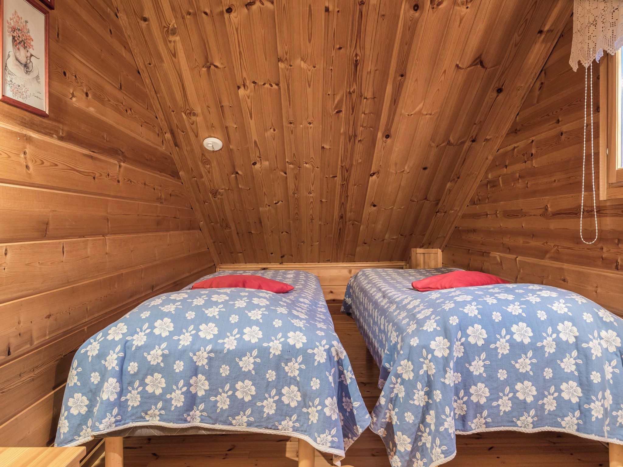 Eine Holzhütte mit zwei Betten, jedes mit einer blumigen Tagesdecke und einem roten Kissen.
