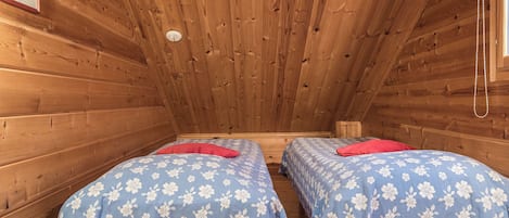 Eine Holzhütte mit zwei Betten, jedes mit einer blumigen Tagesdecke und einem roten Kissen.