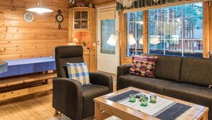 L’intérieur chaleureux d’un chalet avec des murs en bois, une table à manger, un canapé et une fenêtre donnant sur les arbres.
