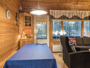 Interior acogedor de una cabaña con una mesa de comedor, un sofá, un ventanal con vistas a árboles y paredes de madera.