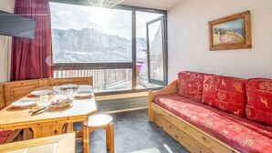 Una stanza con un tavolo in legno apparecchiato per consumare i pasti, un divano rosso, un'ampia finestra con vista sulle montagne e un quadro appeso alla parete.