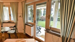 Una stanza con un tavolo da pranzo, sedie, una finestra con tende e vista su un giardino.