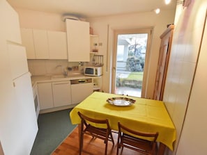 A compact kitchen with white cabinets, a microwave, and a sink. A yellow table with a plate is set for two. - Villa Esperia by Interhome (Merano)