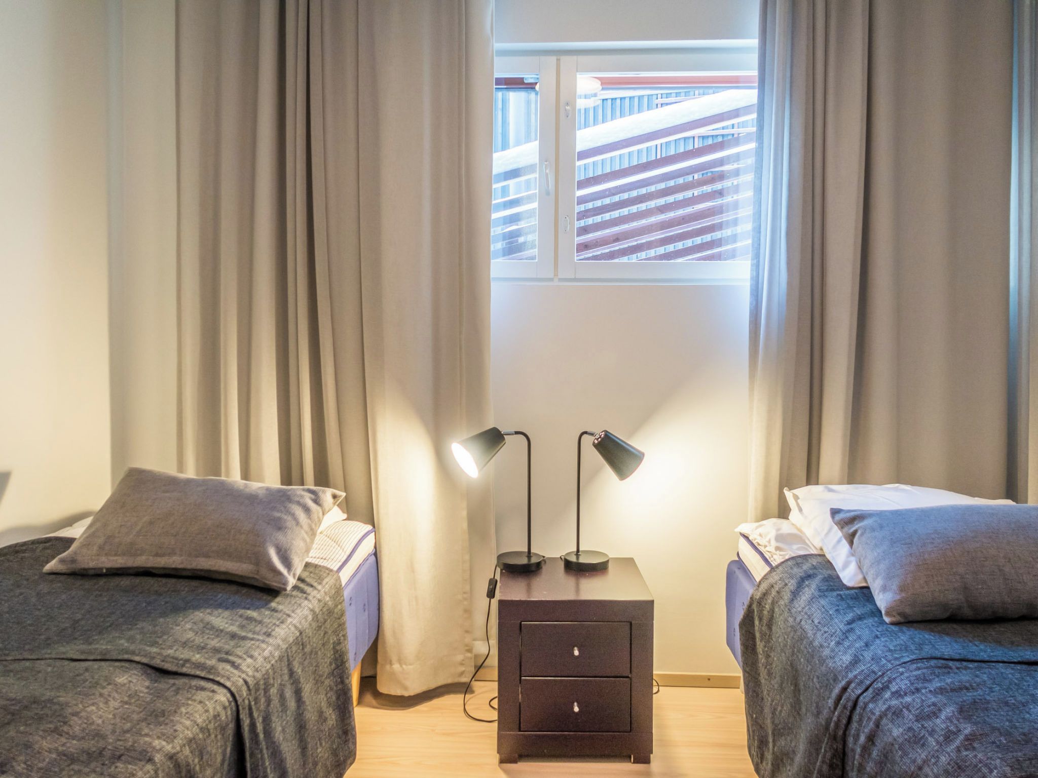 Ein Schlafzimmer mit zwei Betten, einem Nachttisch mit zwei Lampen und einem Fenster mit Vorhängen.