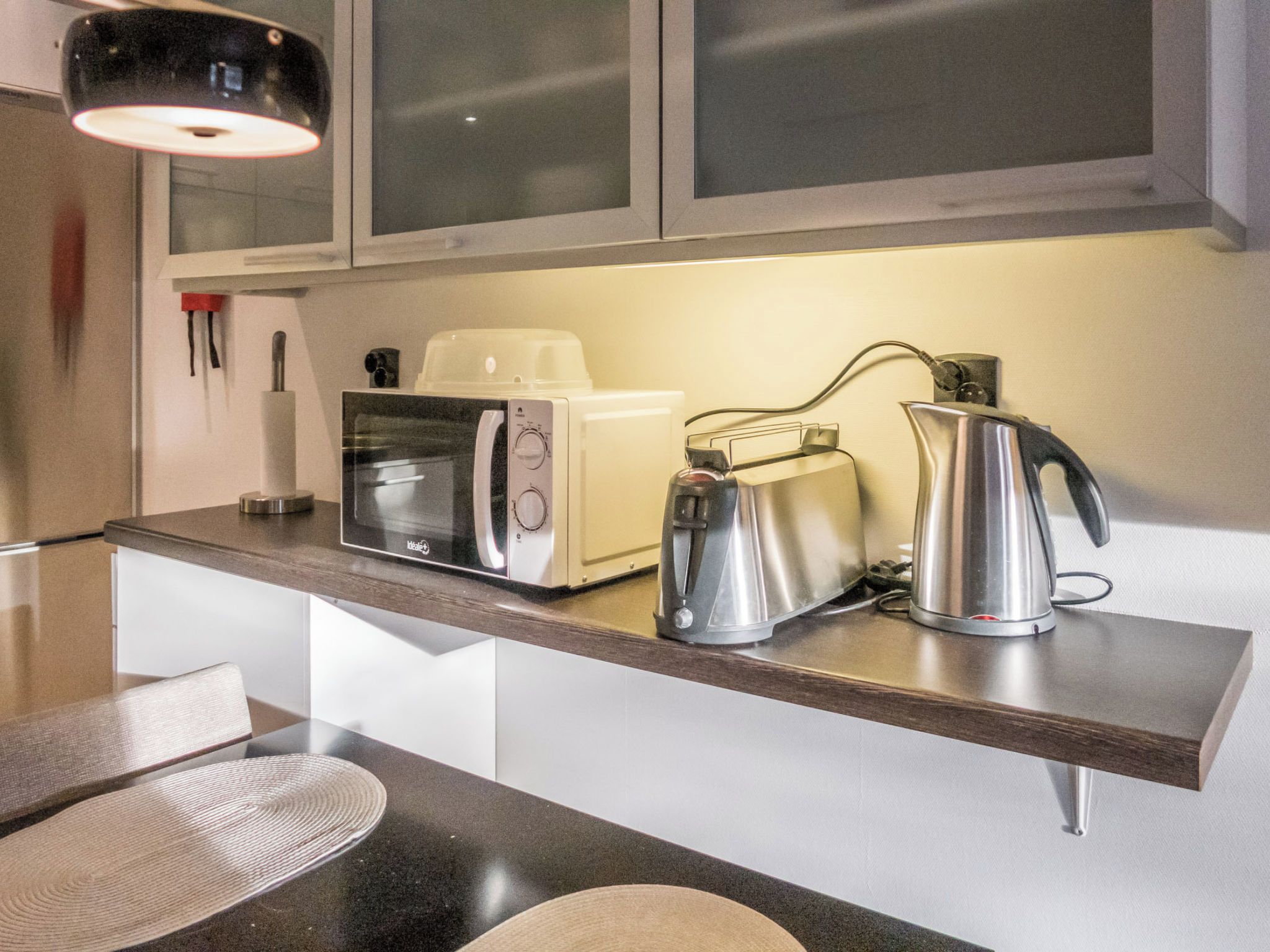Una cocina con microondas, tostadora y hervidor sobre la encimera.