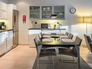 Une cuisine moderne avec un coin repas, des appareils électroménagers en acier inoxydable et une horloge au mur.