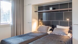 Une chambre moderne avec deux lits, une tête de lit sombre, des lampes de chevet et une fenêtre avec des rideaux.