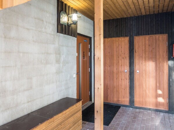 Un banco de madera, una puerta con un número y una pared con un aplique.