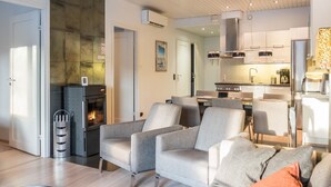 Un salon moderne avec des canapés gris, une cheminée et un coin cuisine équipé d’appareils électroménagers en acier inoxydable.
