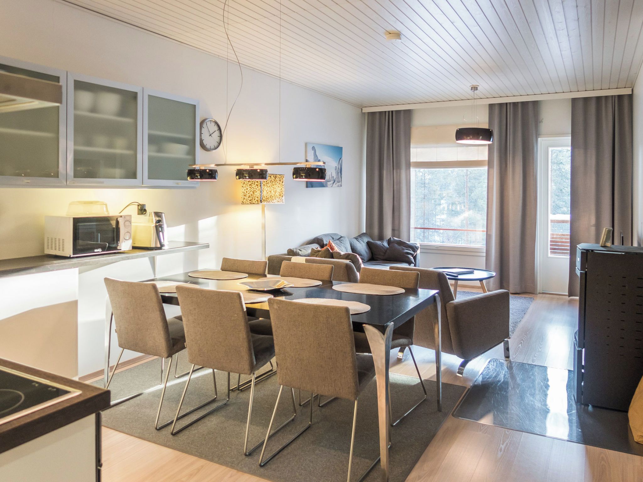 A modern kitchen with a dining area, a sofa, and a view of the outdoors.