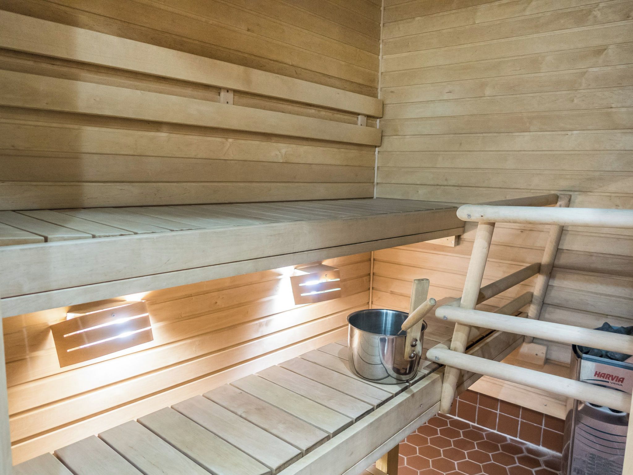 A wooden sauna with a bench, a metal bucket, and a wooden ladder.