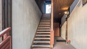 Un escalier en bois mène à un niveau supérieur, avec un mur en béton d’un côté et un plafond en bois de l’autre.