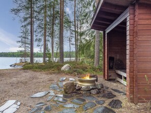 A cabin with a stone fire pit and a view of a lake surrounded by trees.