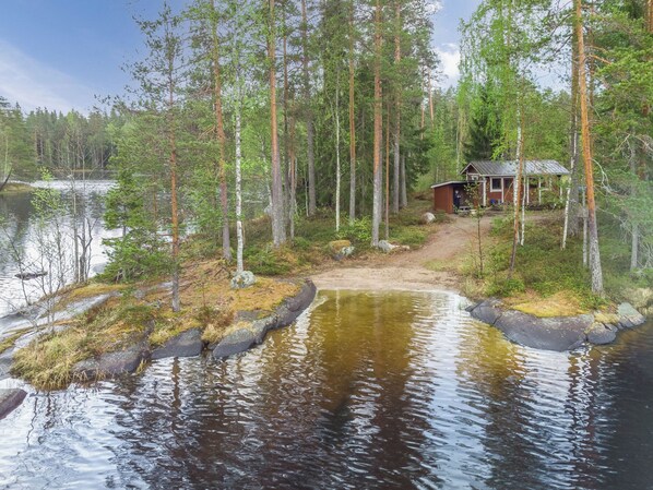 A cabin surrounded by a forest with a small pond in the foreground.