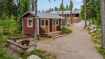 A cabin with a wooden deck, a gravel path leading to it, and a surrounding forest.