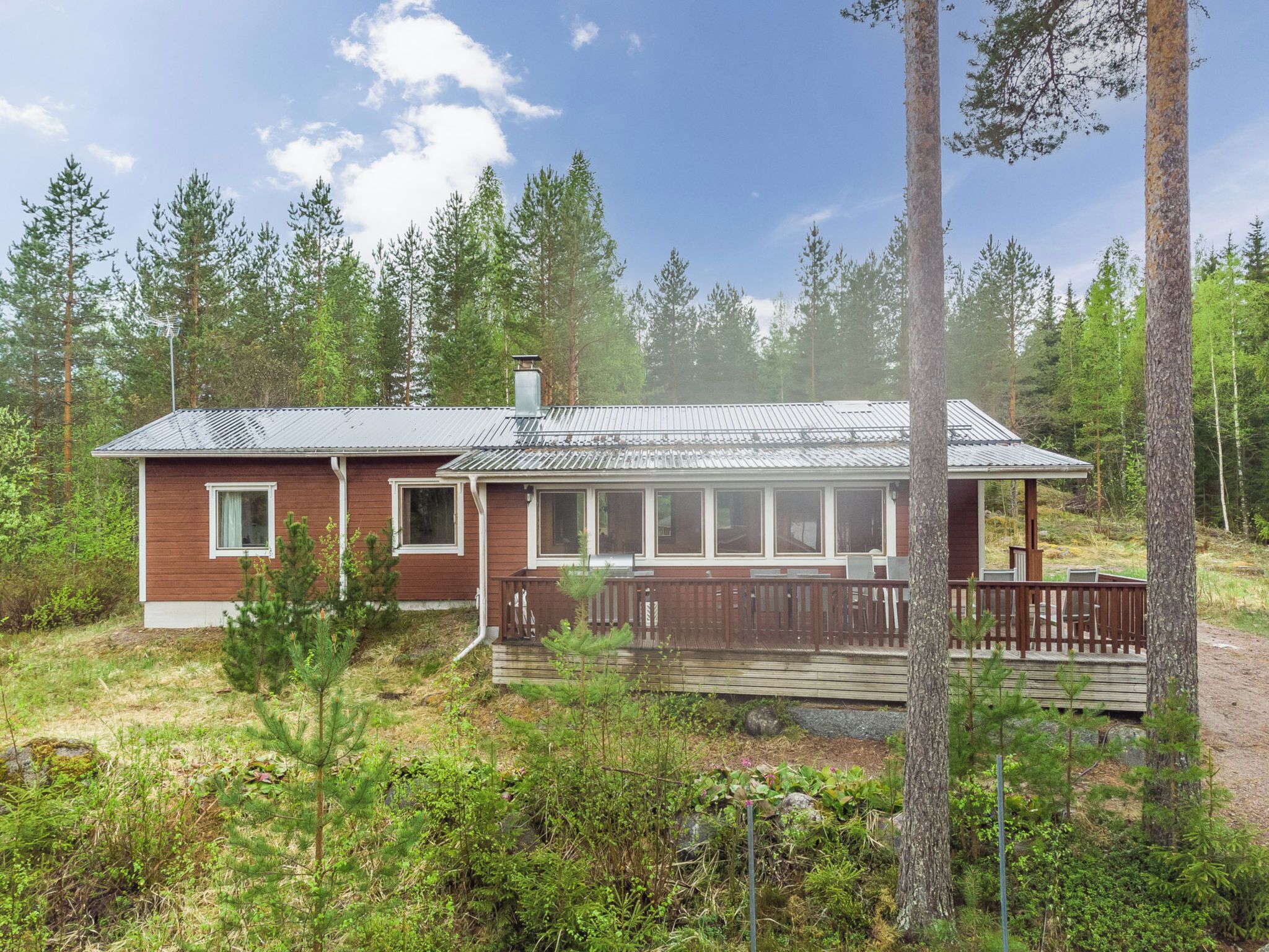 Eine Holzhütte mit Metalldach, einer Holzterrasse und Blick auf den umliegenden Wald.