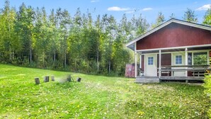 Une cabane rouge avec un porche, entourée d’une pelouse et d’arbres.
