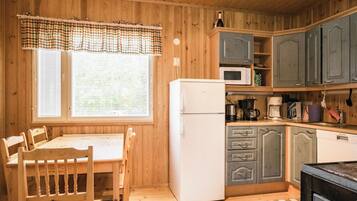 A wooden-paneled kitchen with a white refrigerator, a microwave, and a coffee maker. There is a dining table with chairs and a window with blinds.