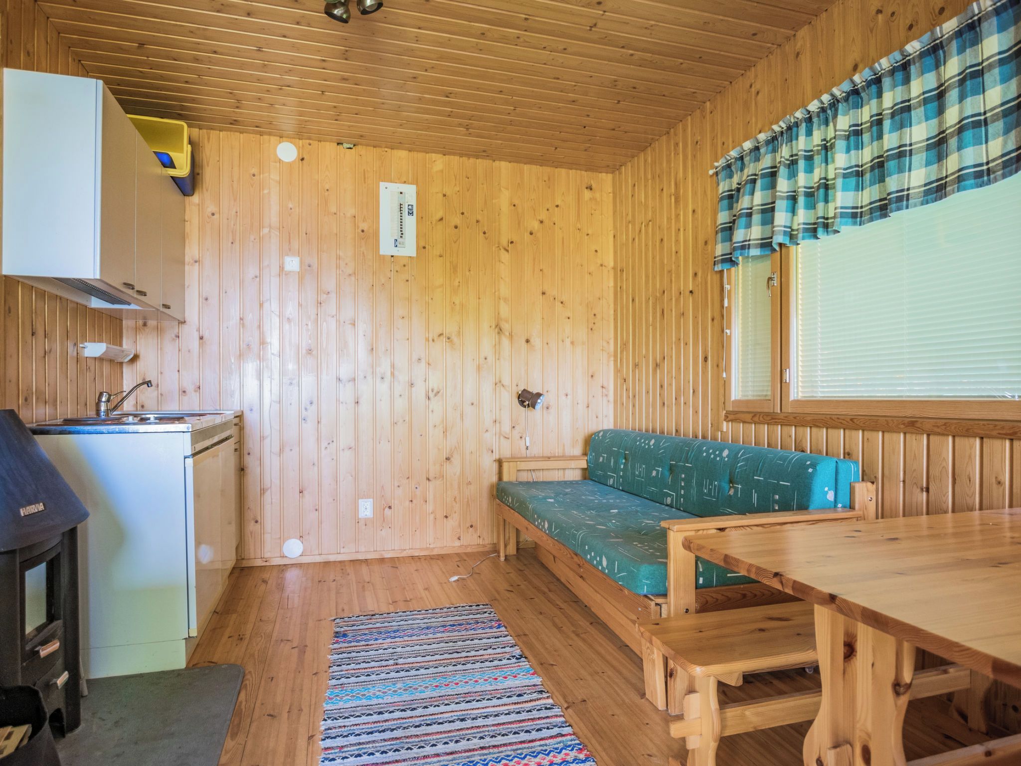 Een compact houten chalet met een kitchenette, een groene bank en een eettafel.