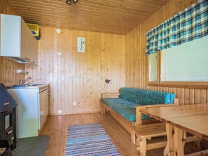 Una cabana de fusta compacta amb petita cuina, un sofà verd i una taula de dinar.