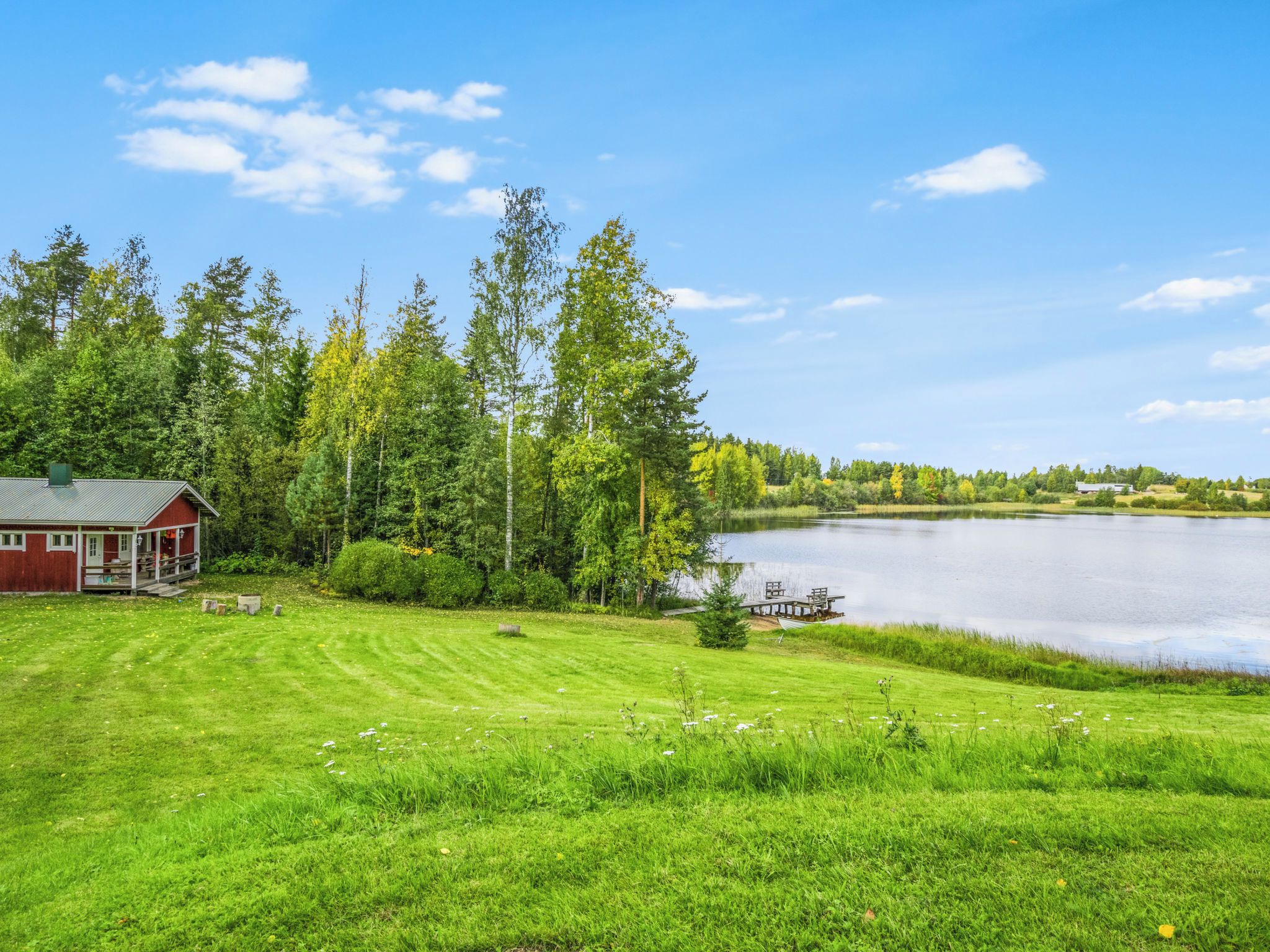 A lakeside property with a red cabin, a dock, and a grassy area.